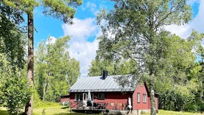 Eine rote Holzhütte mit Veranda, umgeben von Bäumen und Gras.