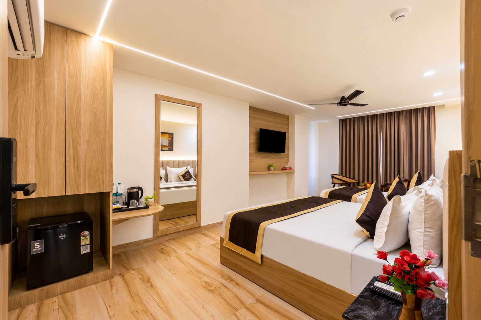 A hotel room with a bed, a desk, a television, a ceiling fan, and a small refrigerator.