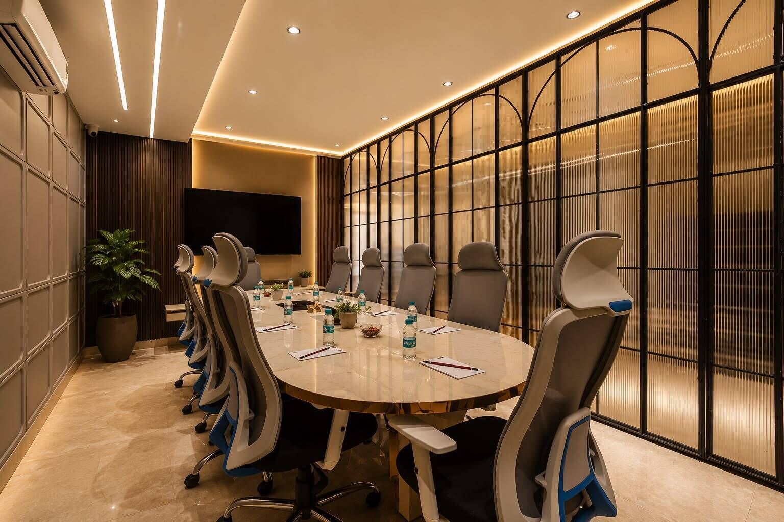 A conference room with a round table, chairs, a TV, and a potted plant.