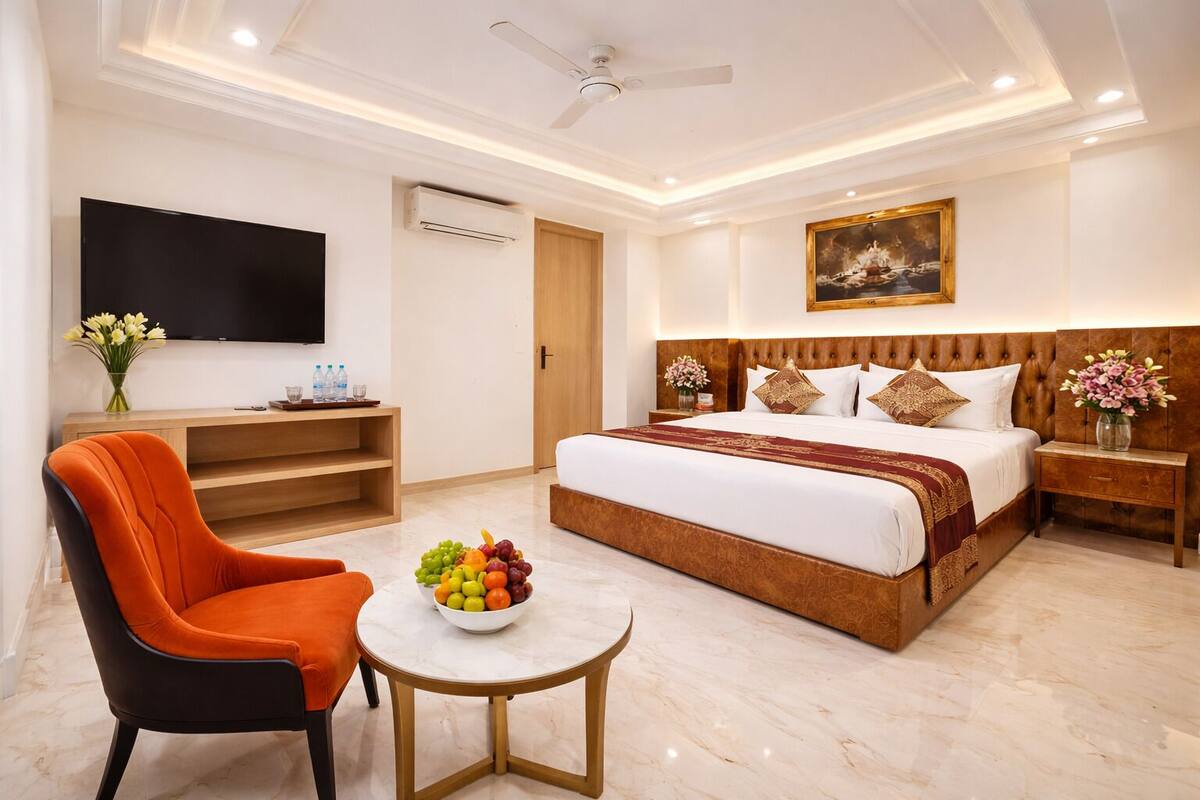 A hotel room with a large bed, a television, a fruit bowl, a chair, and a small table.