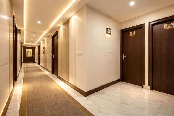 Un couloir d’hôtel avec des portes numérotées 302 et 503, un sol recouvert de moquette et un plafond éclairé.