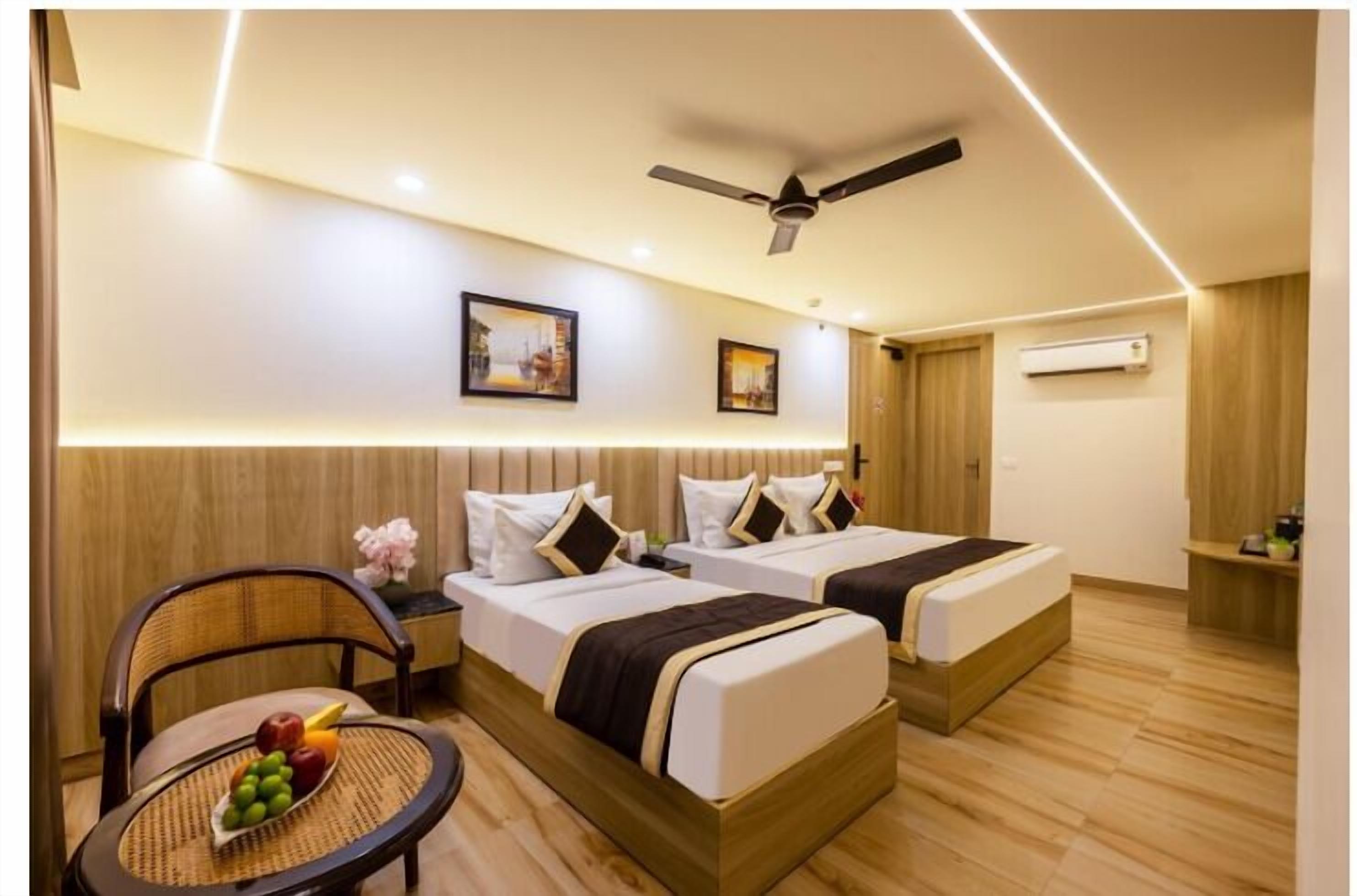 A hotel room with two beds, a ceiling fan, wall-mounted air conditioning, and a small table with fruit.