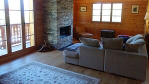 Ein gemütliches Wohnzimmer mit Kamin aus Stein, Holzwänden, einer Couch und einem großen Fenster.