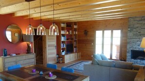 Ein gemütliches Wohnzimmer mit einem Holzesstisch, blauen Stühlen, einem grauen Sofa und einem Kamin aus Stein.