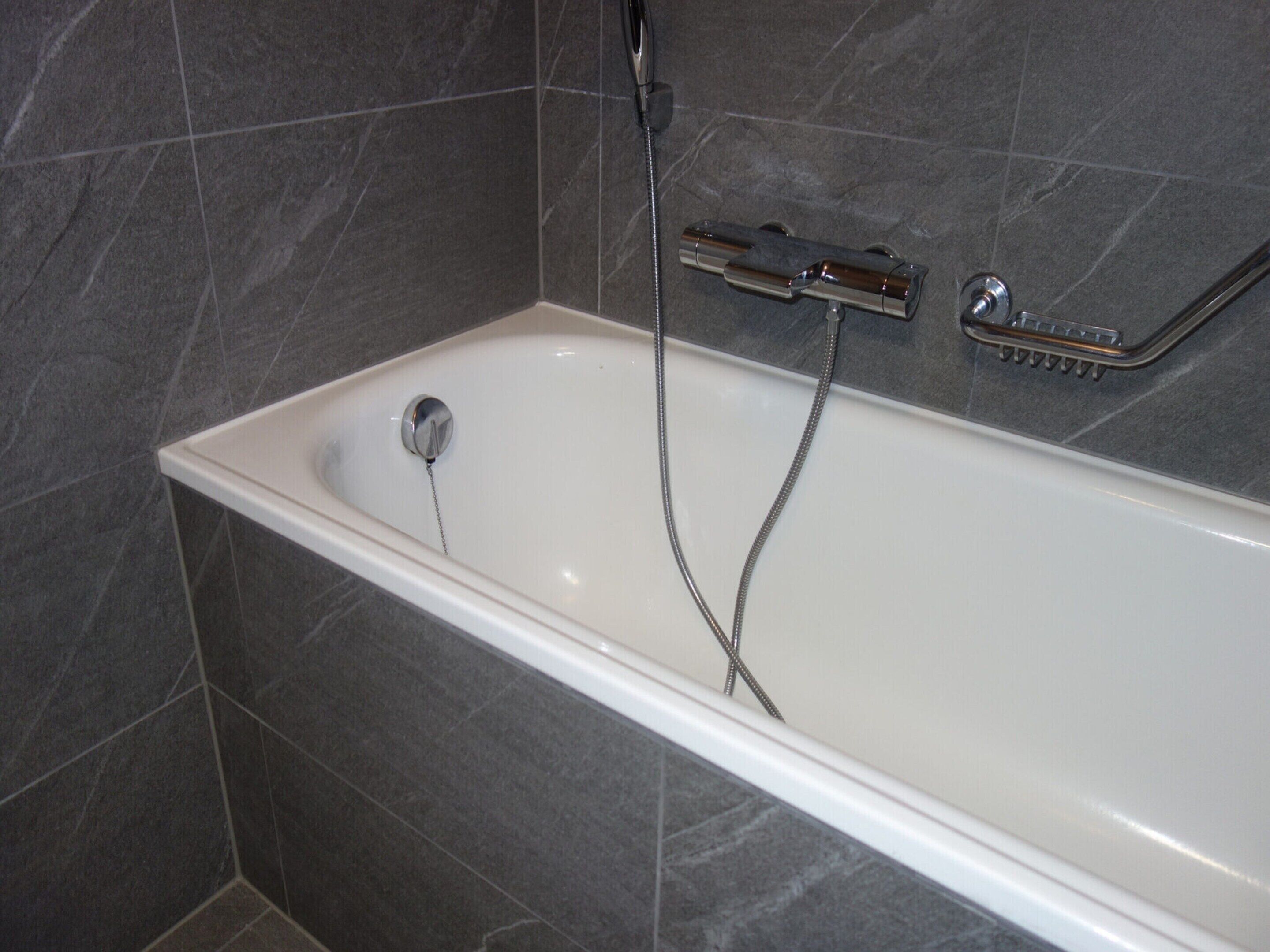 A modern bathroom with a white bathtub, a handheld showerhead, and a wall-mounted faucet.