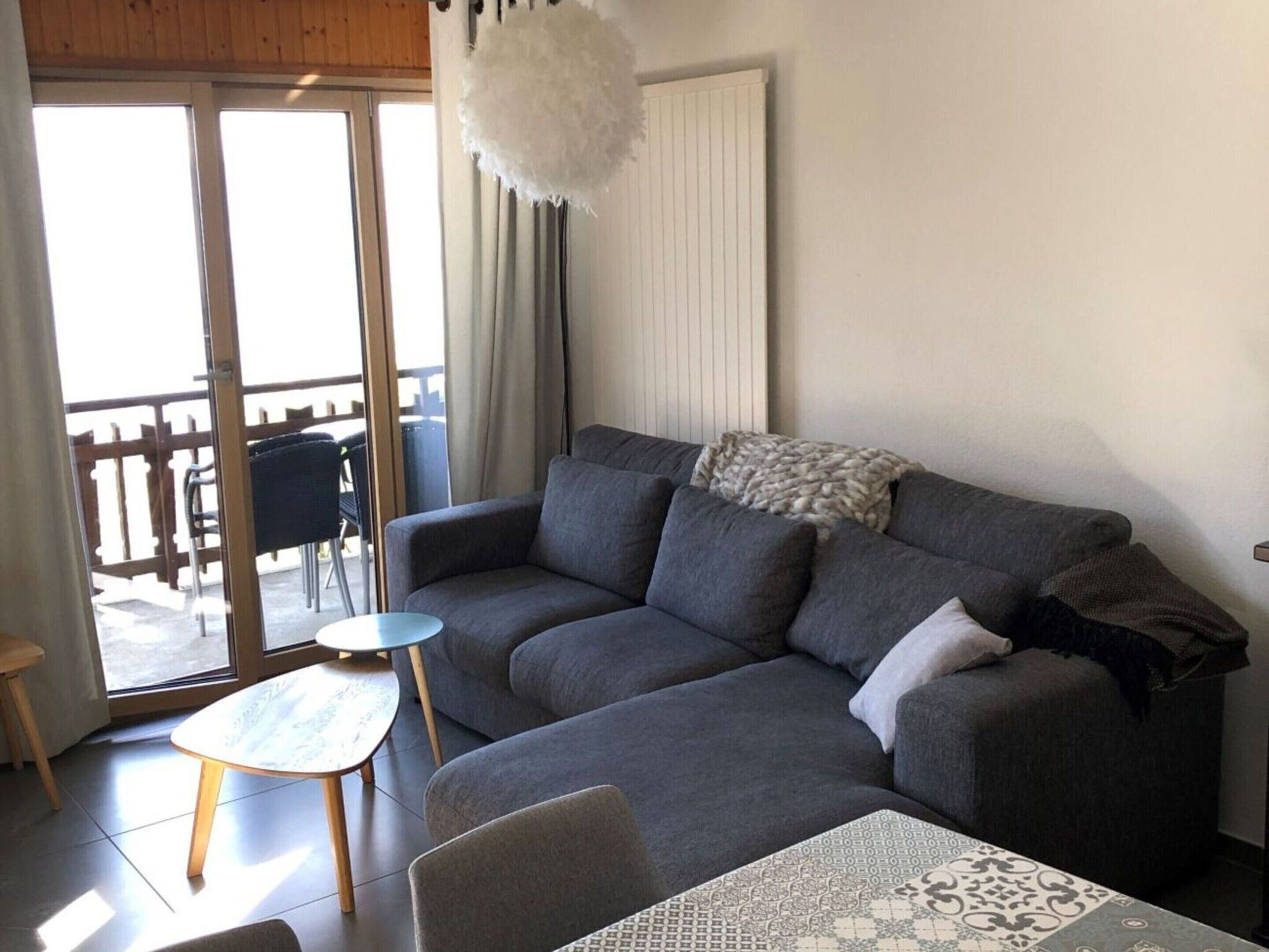 A living room with a grey sofa, a small round table, and a patterned tablecloth.
