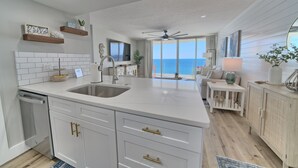 Una cocina moderna con armarios blancos, una isla grande con un lavamanos y vista al océano.