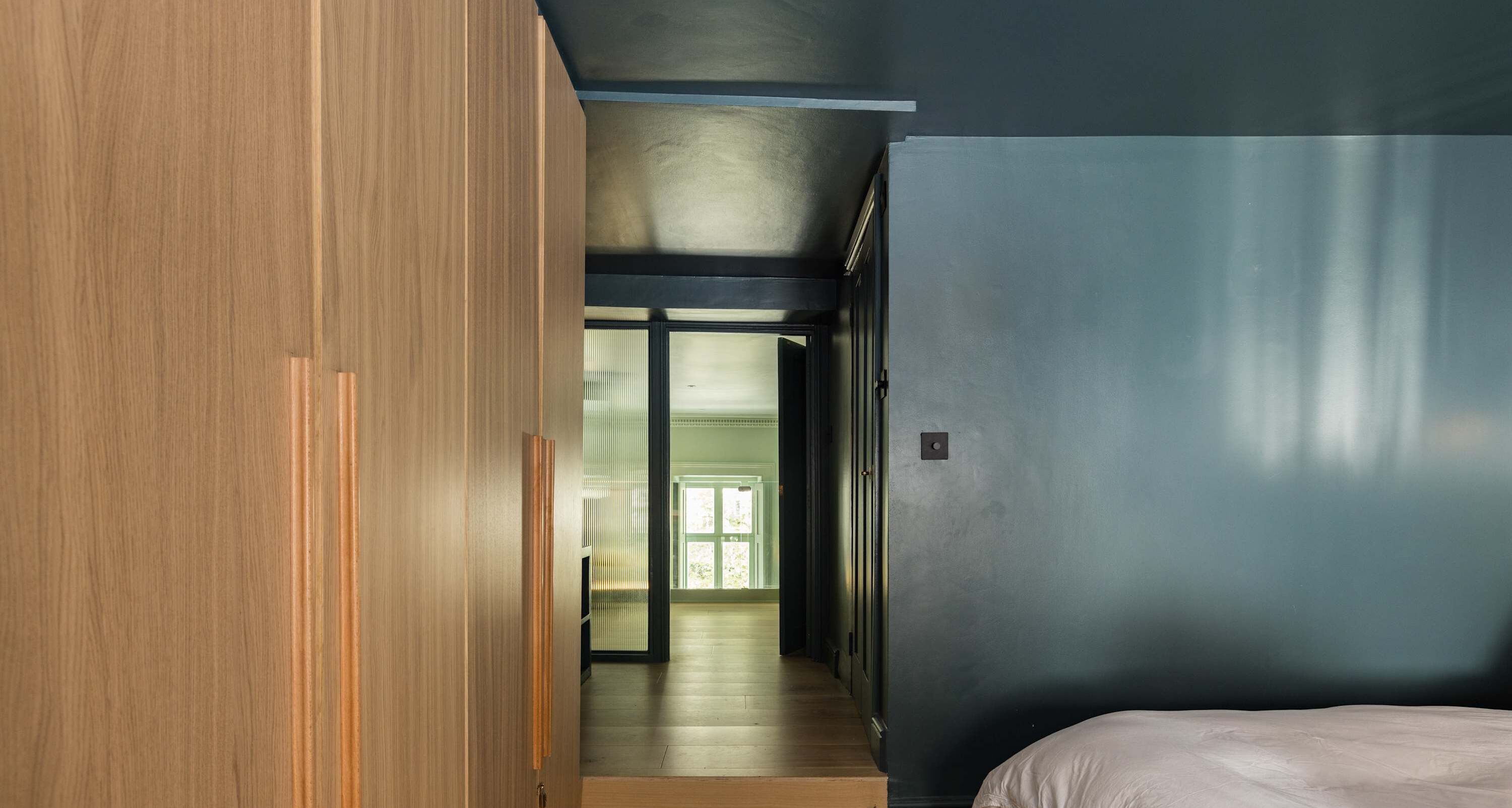 Un dormitorio moderno con una cama grande, un armario de madera y una pared azul oscuro.