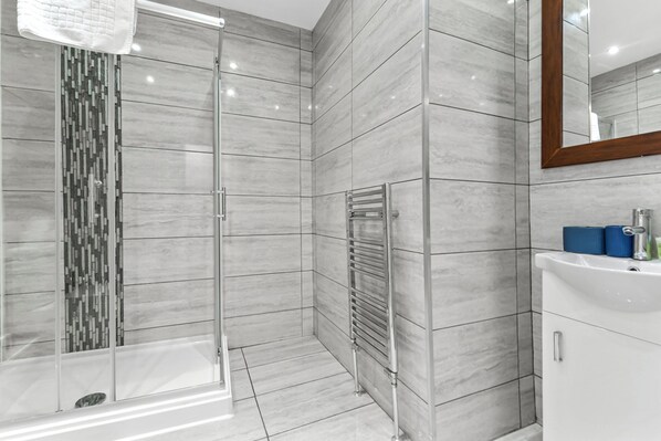 Un baño moderno con cabina de ducha de vidrio, lavamanos empotrado y espejo con marco de madera.