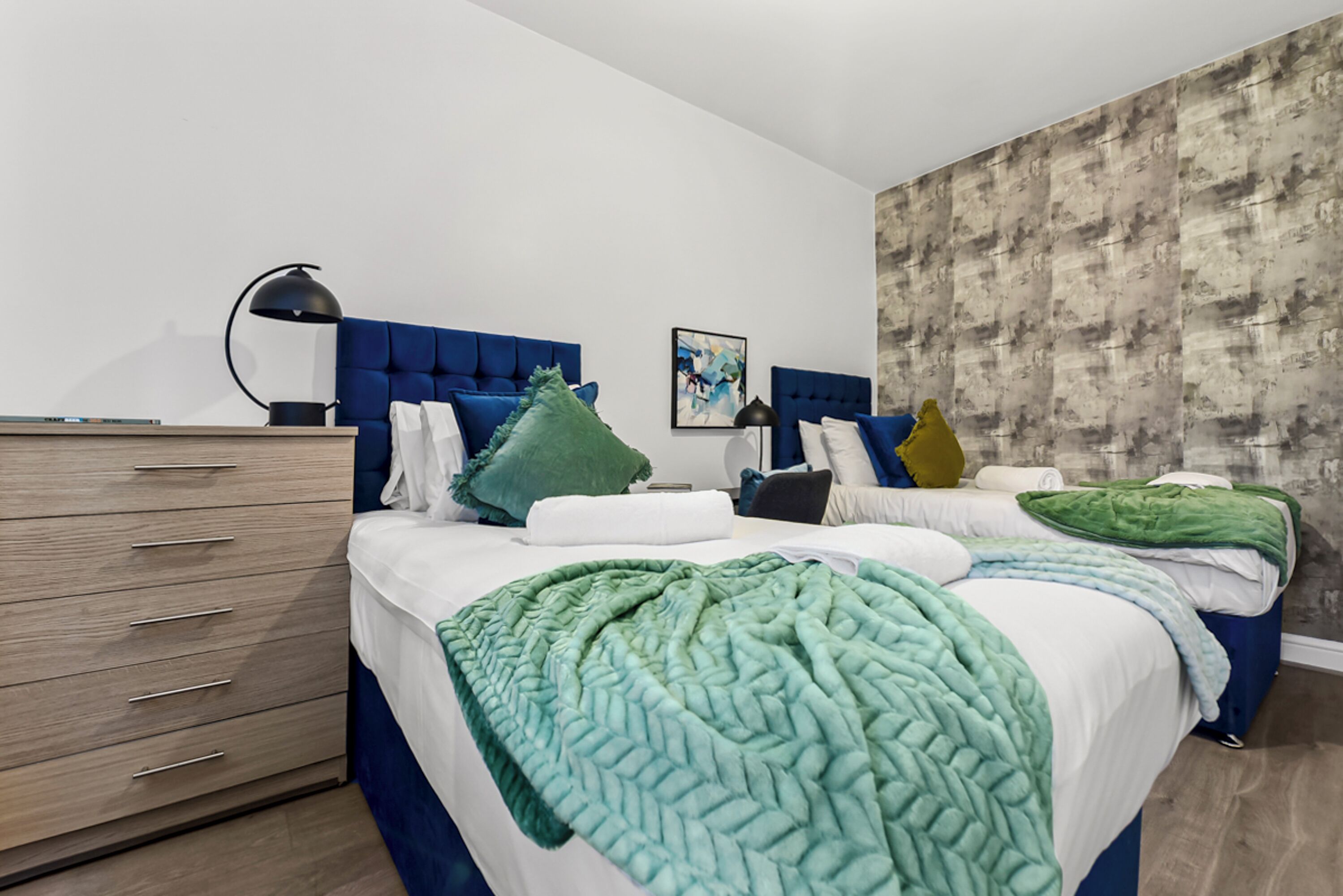 Un dormitorio moderno con un cabecero azul, un aparador de madera y una pared gris con textura.
