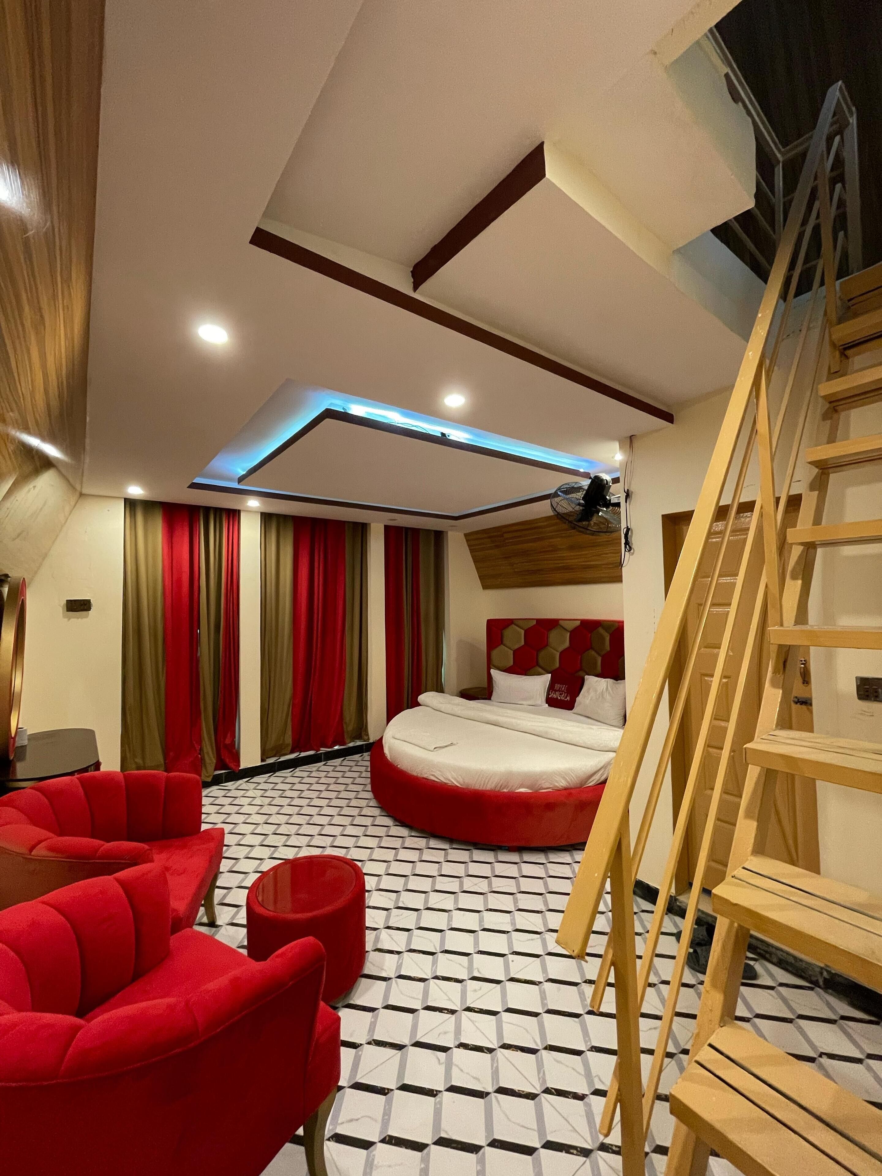 A modern bedroom with a large bed, red furniture, a wooden ladder, and a skylight.