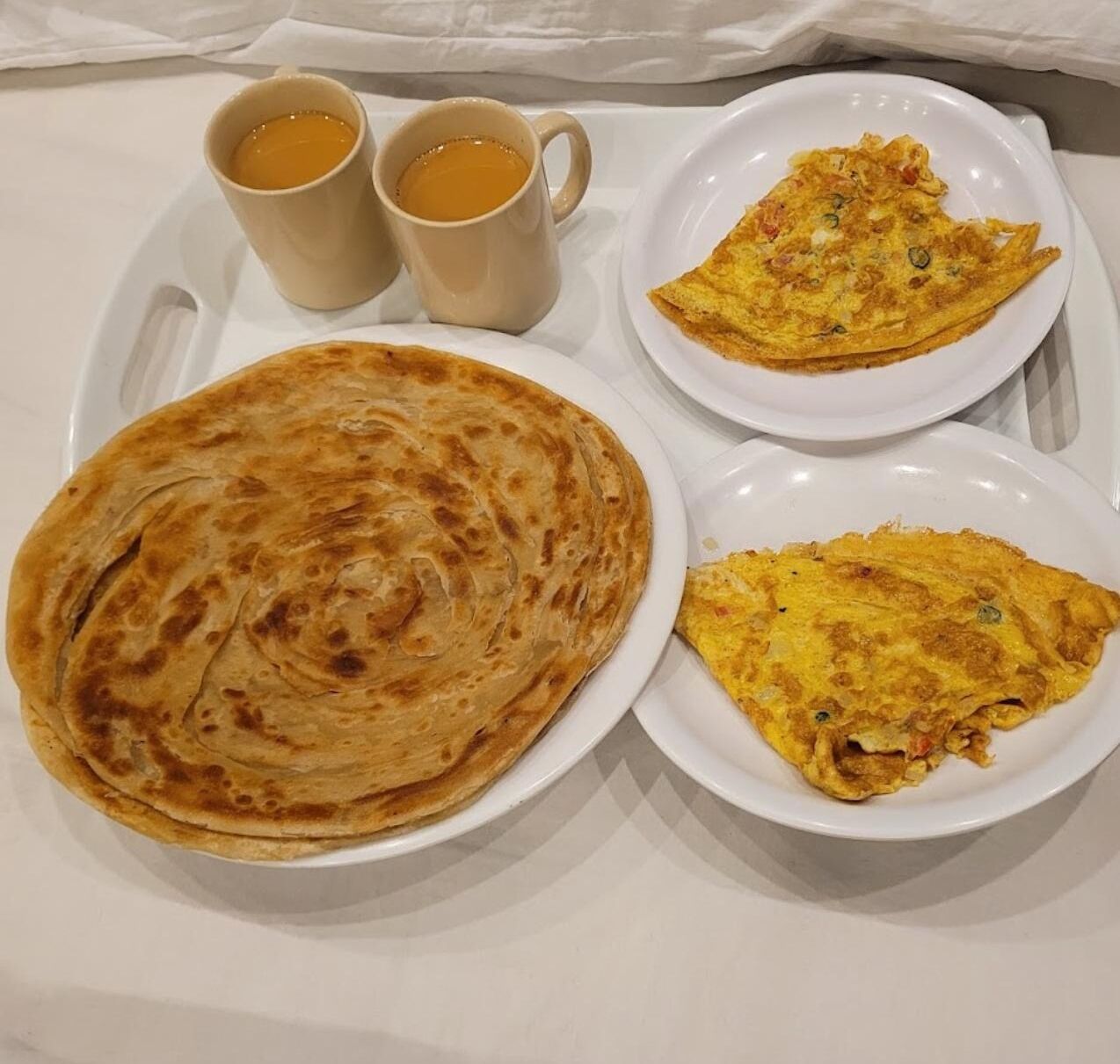 A breakfast tray with a folded flatbread, two cups of coffee, and two plates of omelette.