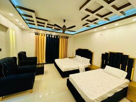 Habitación de hotel con dos camas, un ventilador de techo y una zona de estar con un sofá negro.