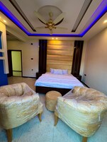 Un dormitorio moderno con una cama grande, dos sillones tapizados, un otoman redondo e un ventilador de techo.