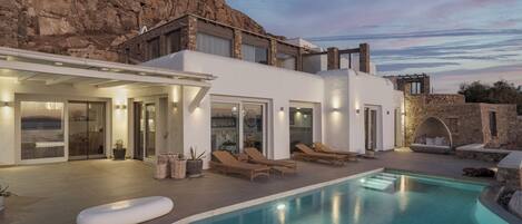 A modern villa with a swimming pool, outdoor seating, and a view of rocky terrain.