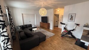 A living room with a sectional sofa, a TV, a ceiling light, and a stationary bike.