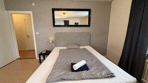 A hotel room with a bed, a nightstand, a lamp, a mirror, and a door.