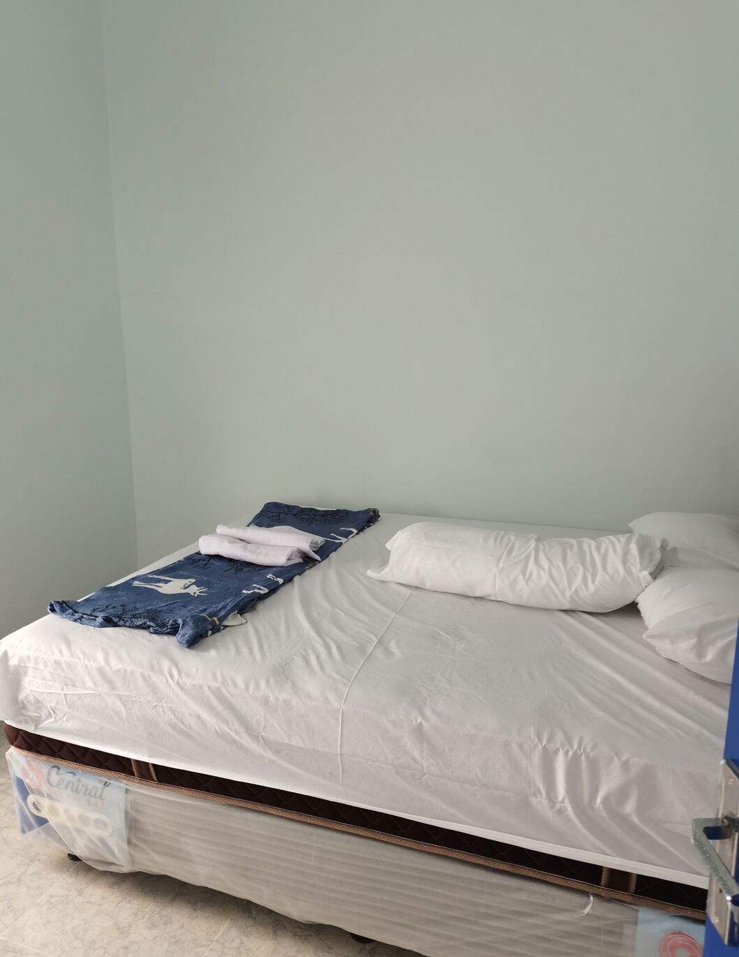 Un lit simple avec du linge de lit blanc, une couverture bleue et un oreiller.