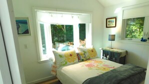 A bedroom with a bed, a window with blinds, a bedside table with a lamp, and a framed picture on the wall. - Bright and cozy private cottage (CS0037) (Wellfleet)