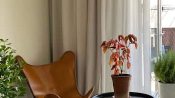 Um quarto com uma poltrona de couro marrom, uma mesa redonda pequena com uma planta em vaso e uma janela com cortinas.