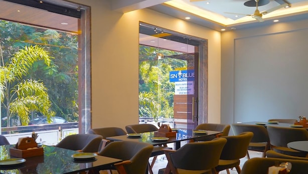 Une salle de conférence d’hôtel avec des tables et des chaises en verre, de grandes fenêtres donnant sur un paysage verdoyant et un panneau indiquant « SN BLUE HOTEL ».