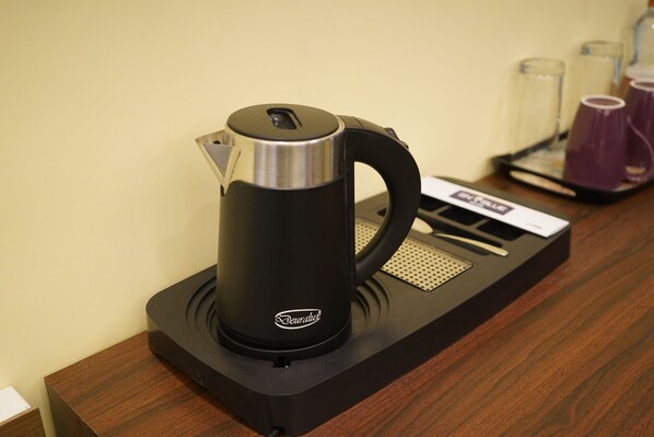 A De'Longhi electric kettle on a wooden countertop with a tray holding purple cups and a card.