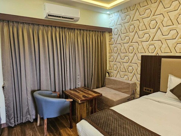 A hotel room with a bed, a small table, a chair, and a curtain.
