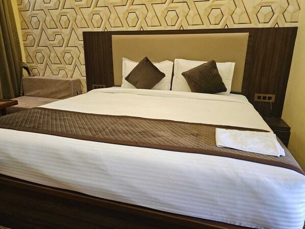 A hotel room with a large bed, a wooden headboard, and a patterned wall.