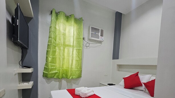 Habitación de hotel con cama, televisor en un estante, cortina verde y pared blanca.