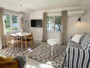 Un salon comprenant un canapé, un téléviseur, une table à manger avec des chaises et une petite table blanche.