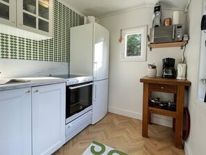 Une cuisine compacte avec des meubles blancs, un four encastré, un four à micro-ondes et une machine à café placés sur une étagère en bois.
