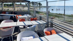 An outdoor seating area with tables and chairs, overlooking a beach and the sea. - 4 Star Holiday Home in Farjestaden (Farjestaden)