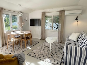 A living room with a sofa, a TV, a dining table with chairs, and a small white table.
