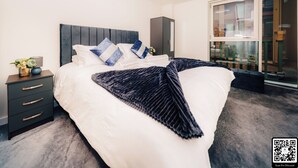 A modern bedroom with a large bed, dark headboard, and a view of a cityscape through a large window. - -15% LUX Riverside Duplex Masionette By LCY/ExCeL I 25min to Tower of London (London)