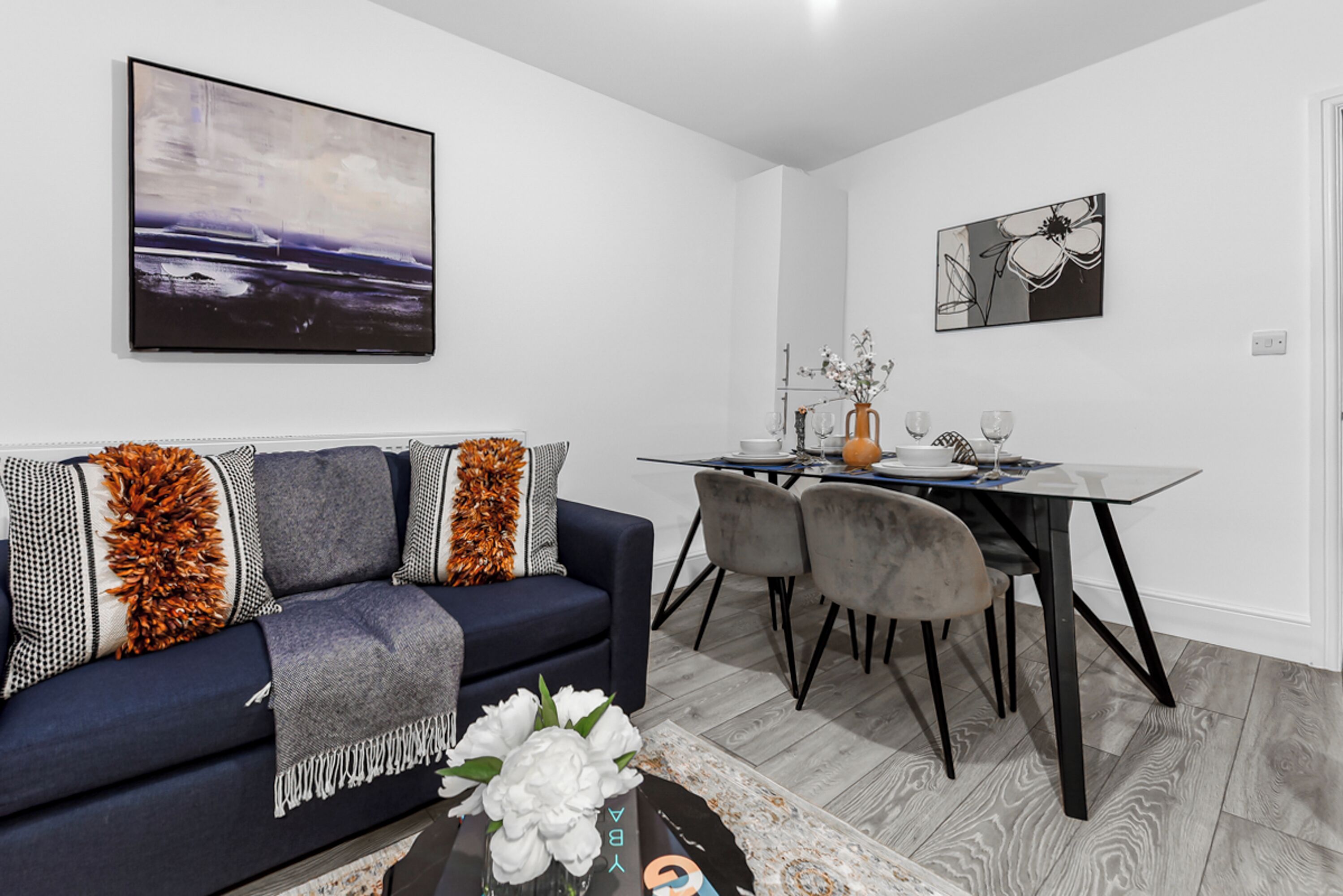 A modern living room with a dark blue sofa, a glass coffee table, and a dining area with a glass table and chairs.