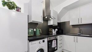 A modern kitchen with white cabinets, a built-in washing machine, an oven, and a stainless steel range hood.
