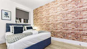A modern bedroom with a brick wall, a bed with a blue headboard, and a wooden floor.
