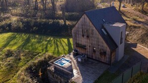 A large, rustic barn-style building with a sloped roof, a patio area with a hot tub, and a surrounding natural landscape. - Beautiful Villa With Spacious Rooms (Lešany)