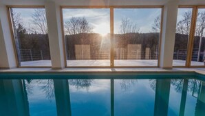 A swimming pool with clear reflections, large windows, and a view of trees and a building in the background. - Tranquil Villa With Nature Access (Mala Moravka)