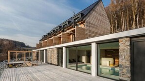 A modern building with a wooden deck, large glass windows, and a stone accent wall. - Tranquil Villa With Nature Access (Mala Moravka)