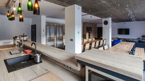A modern kitchen with a long countertop, stainless steel appliances, and hanging pendant lights. - Tranquil Villa With Nature Access (Mala Moravka)