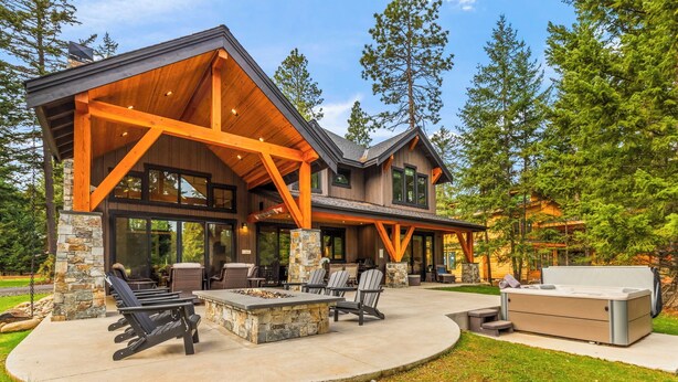 Une maison moderne dotée d’un patio couvert, de piliers en pierre et d’un grand espace extérieur aménagé pour se détendre.