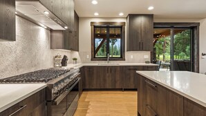 Une cuisine moderne avec des meubles en bois foncé, une cuisinière en acier inoxydable et une grande fenêtre donnant sur l’extérieur.