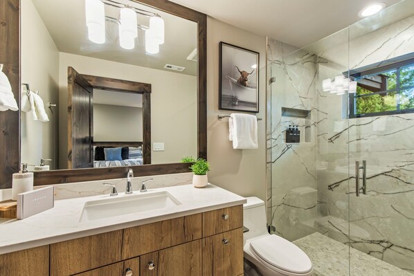 A modern bathroom with a marble sink, wooden vanity, a large mirror, a glass shower enclosure, and a framed picture on the wall.