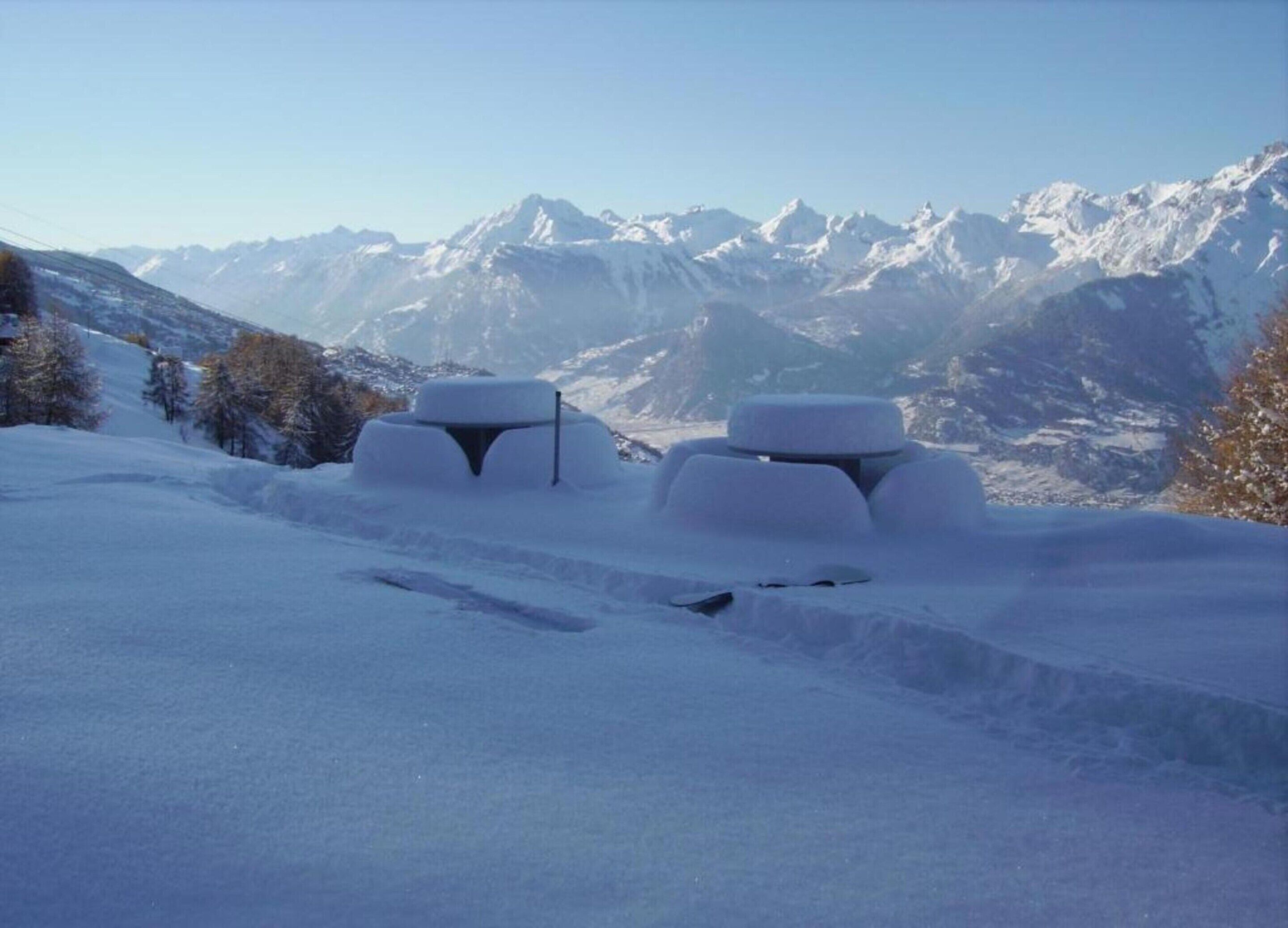 A snow-covered landscape with two snow mounds and a mountain range in the background.