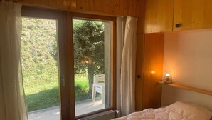 A bedroom with a bed, a window with curtains, a radiator, and a wall-mounted light. - Classy Apartment Amid Hills (Veysonnaz)