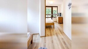 A bedroom with a wooden floor, a bed, a dresser, and a window with a view of greenery. - Spacious Villa With Lush Garden (Harrachov)