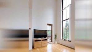 A spacious room with a large window, a flat-screen TV, wooden flooring, and a grey rug. - Spacious Villa With Lush Garden (Harrachov)
