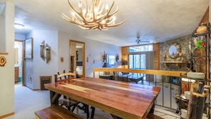 Un espace repas avec une grande table en bois et des bancs, un lustre et une cheminée en pierre.