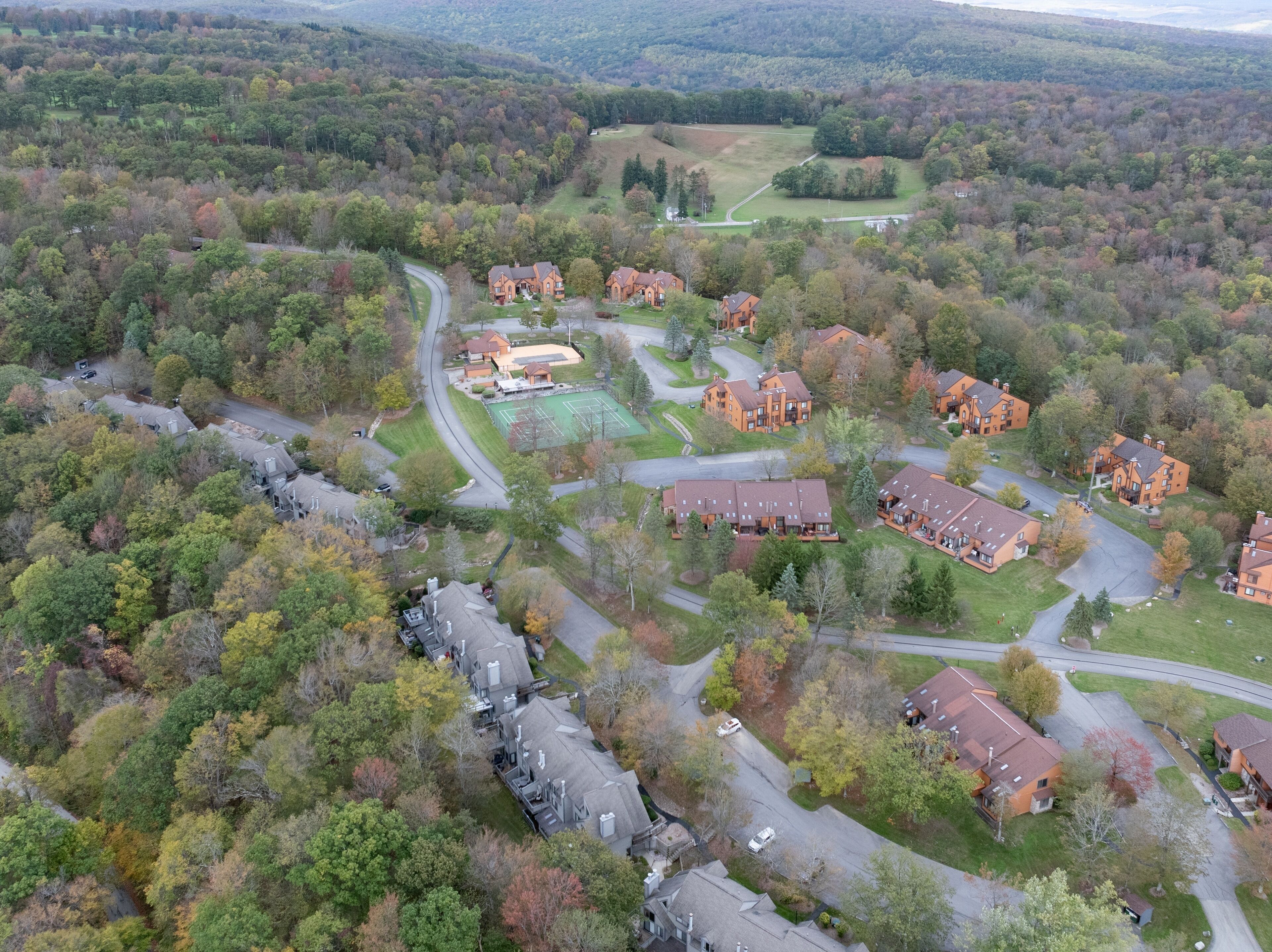 Vista aérea de una zona residencial con varias casas, calles y una cancha de tenis.